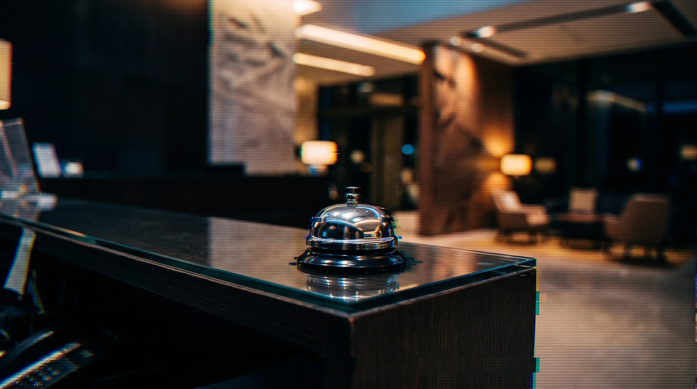 Digital illustration for article section "Why Hotels Might Finally Bite" in "Semi-Humanoid Robots Enter Hotel Kitchens as Labor Crunch Persists" - A sleek, modern hotel reception desk featuring a solitary, polished silver service bell as the centr...